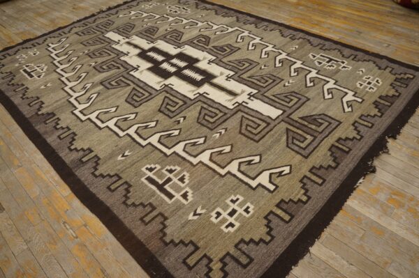 Geometric rug in neutral taupe, dark brown, and cream with a low pile on distressed wood flooring.