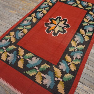Red flatweave rug featuring a geometric medallion and multicolored floral border on rustic wood flooring.