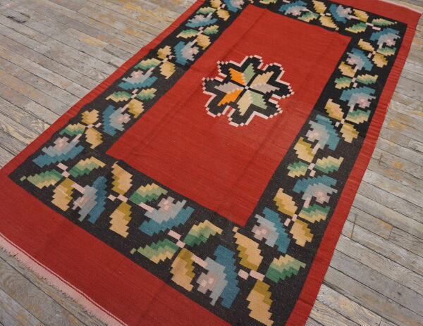 Red flatweave rug featuring a geometric medallion and multicolored floral border on rustic wood flooring.