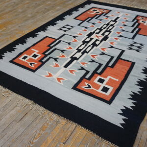 Black and terracotta geometric flatweave rug with light blue field and fringe on rustic wood flooring.