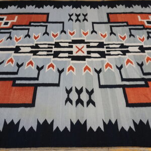 Low-pile rug with geometric patterns in light blue, black, rust red, and white on wood planks.