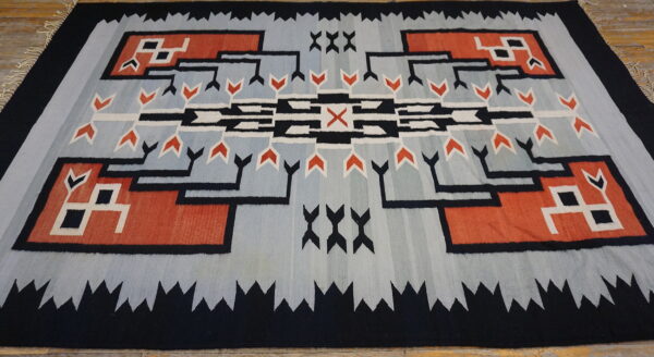 Low-pile rug with geometric patterns in light blue, black, rust red, and white on wood planks.