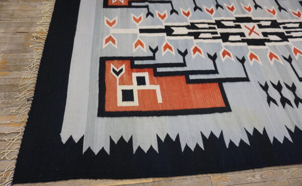 Flatweave rug in black, pale blue, orange, and white geometric patterns rests on distressed wood flooring.