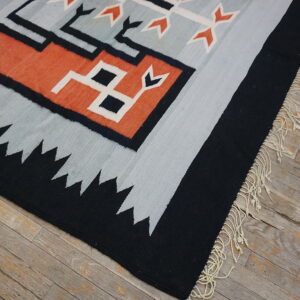 Gray, black, and terracotta geometric flatweave rug with fringe lies on rustic wood planks.