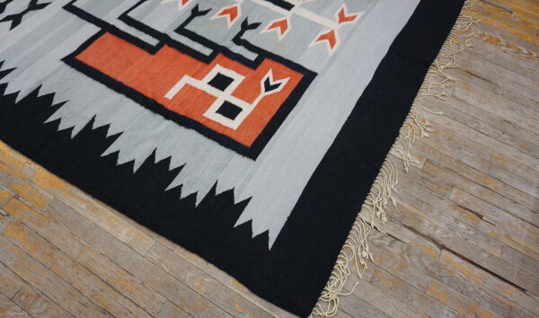 Gray, black, and terracotta geometric flatweave rug with fringe lies on rustic wood planks.