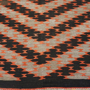 Flatwoven geometric rug with interlocking black, orange, and gray patterns displayed on wood flooring.
