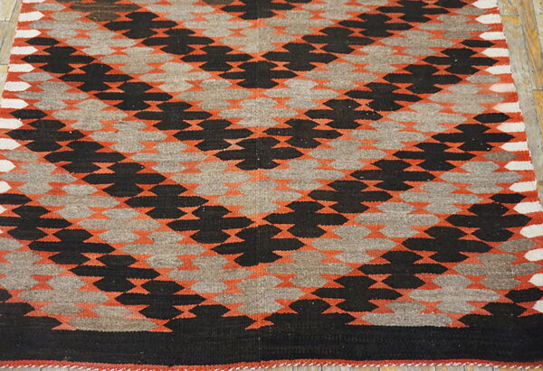 Flatwoven geometric rug with interlocking black, orange, and gray patterns displayed on wood flooring.