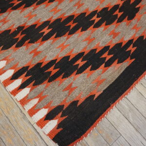 Flatweave rug with black, rust orange, gray, and white serrated diamond patterns on rustic wood floor.