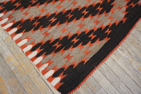 Flatweave rug with black, rust orange, gray, and white serrated diamond patterns on rustic wood floor.