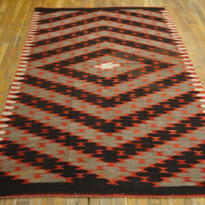 Runner rug with black, gray, and orange geometric diamond pattern on a worn yellow wooden floor.