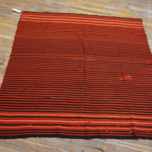 Flatweave rug with alternating black and red horizontal stripes lying on worn wooden floorboards.