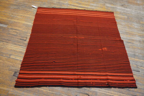 Flatweave rug with alternating black and red horizontal stripes lying on worn wooden floorboards.