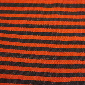 Close-up of a flatweave rug with horizontal orange and black stripes on light wooden planks.