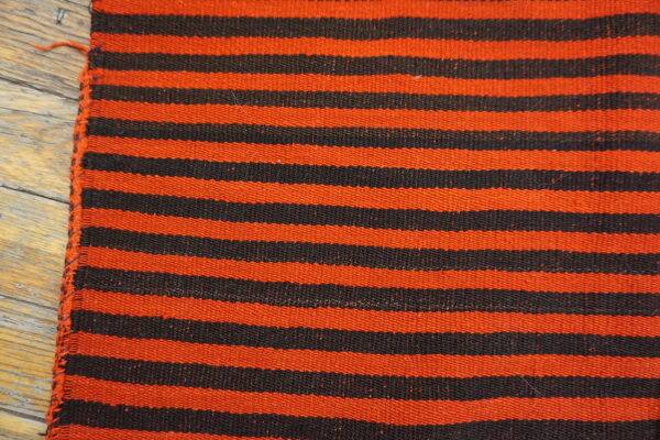 Close-up of a flatweave rug with horizontal orange and black stripes on light wooden planks.