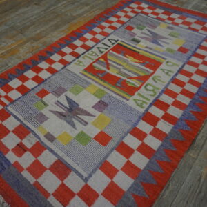 A vibrant flatweave rug with a red checkered border and colorful geometric panels rests on distressed wood flooring.