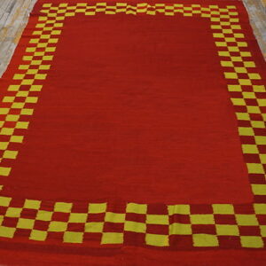 Red flatweave rug with a thick yellow and red checkered border rests on light wood planks.