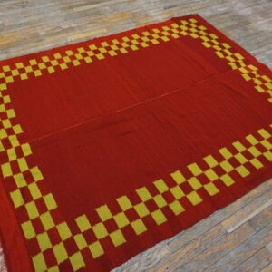 Red flat-weave rug featuring a bold yellow-green checkerboard border on distressed wood planks.