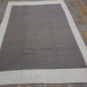 Low-pile gray and off-white rug with a sawtooth inner border rests on distressed wooden floorboards.