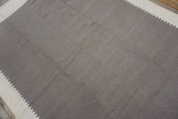 Simple taupe flatweave rug featuring stepped cream borders on distressed wood flooring.