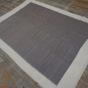 Flatwoven gray rug with a cream border defined by a serrated saw-tooth pattern on weathered wooden planks.