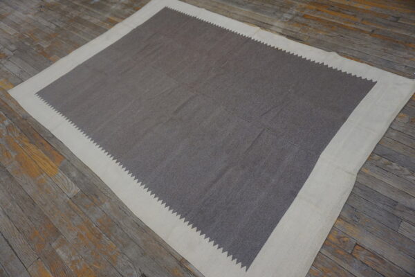 Flatwoven gray rug with a cream border defined by a serrated saw-tooth pattern on weathered wooden planks.