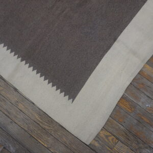 A dark brown and light beige flat rug with a zigzag border rests on rustic wood planks.