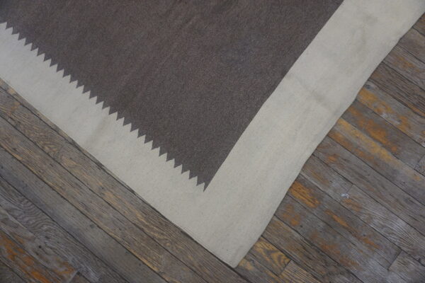 A dark brown and light beige flat rug with a zigzag border rests on rustic wood planks.