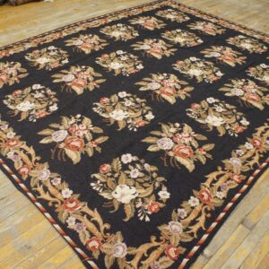 Dark blue rug with large floral bouquets and ornate tan borders on distressed light wood flooring.