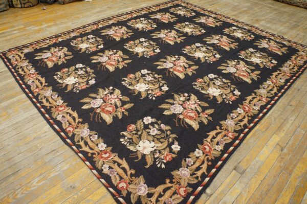 Dark blue rug with large floral bouquets and ornate tan borders on distressed light wood flooring.