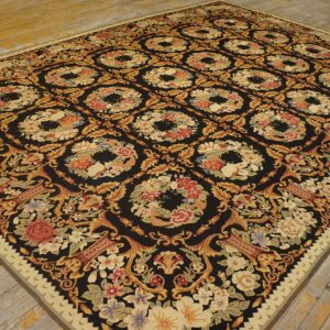Low-pile black rug with dense gold and red floral medallions rests on rustic plank wood flooring.