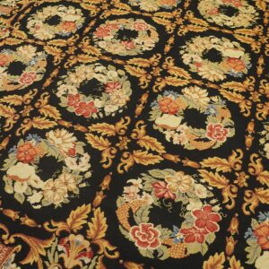 Black rug with repeating floral wreaths and scrolling gold leaves in red, cream, and yellow.