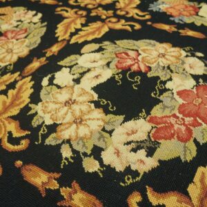 Low-pile rug texture displays intricate floral and leaf patterns in warm colors contrasting with a black background.