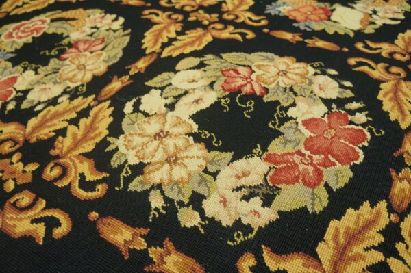 Low-pile rug texture displays intricate floral and leaf patterns in warm colors contrasting with a black background.