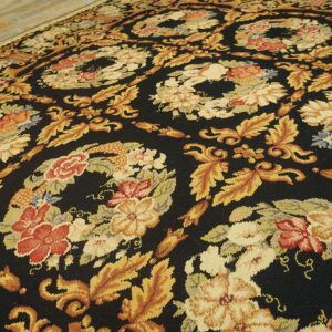 Close-up of a dark floral flat weave rug featuring gold foliage and red flowers on light wood flooring.