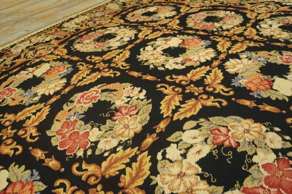 Close-up of a dark floral flat weave rug featuring gold foliage and red flowers on light wood flooring.