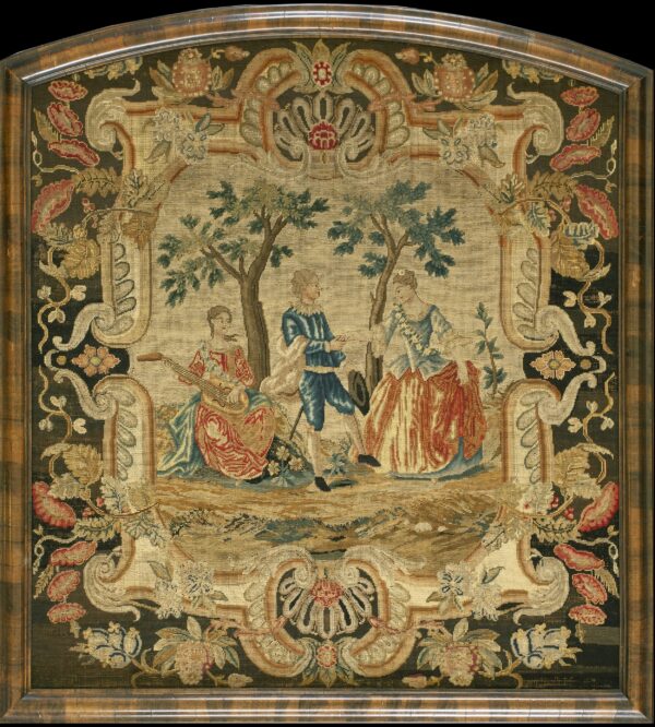 Needlework tapestry framed in wood, featuring a light pastoral scene surrounded by a dense, dark green floral border.