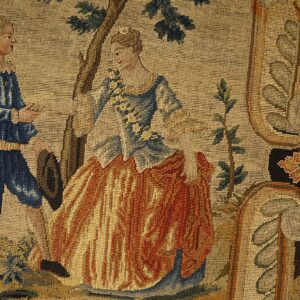 Low pile tapestry rug detail showing blue and orange figures standing near a tree and floral border.