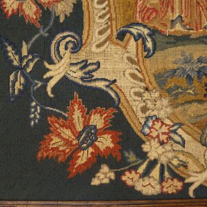 Close-up of a framed, flat-woven textile displaying stylized florals in cream, rust, and blue on dark green.