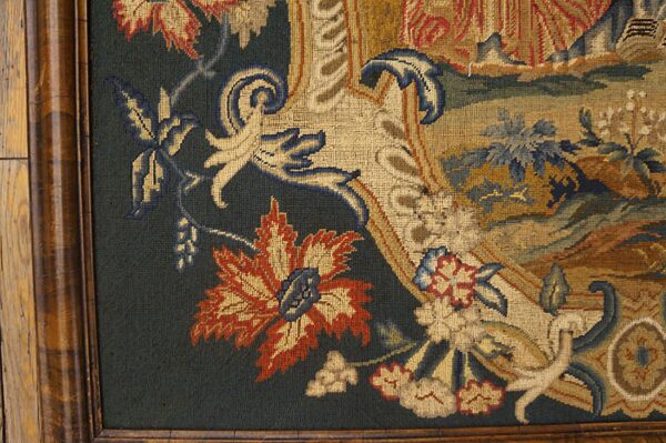 Close-up of a framed, flat-woven textile displaying stylized florals in cream, rust, and blue on dark green.