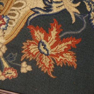 Low-pile needlepoint rug detail featuring rust, gold, and blue foliate designs framed by polished wood.