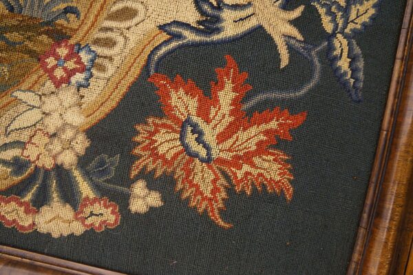 Low-pile needlepoint rug detail featuring rust, gold, and blue foliate designs framed by polished wood.
