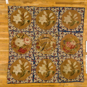 Flatweave rug with a nine-square floral medallion design in tan, blue, and cream on a wood floor.