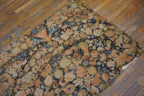Low-pile rug with dense pink, cream, and blue floral motifs on a brown field over wood flooring.