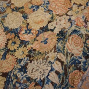 Heavily worn flatweave rug fragment with stitched repairs and muted blue, pink, and tan floral patterns.
