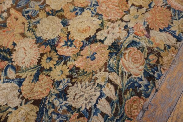Heavily worn flatweave rug fragment with stitched repairs and muted blue, pink, and tan floral patterns.