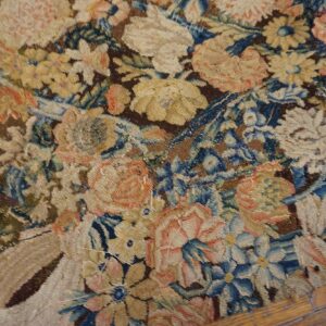 Muted floral tapestry rug in blue, brown, and yellow shown on distressed wood floor.