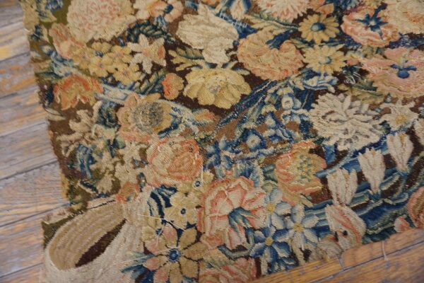 Muted floral tapestry rug in blue, brown, and yellow shown on distressed wood floor.