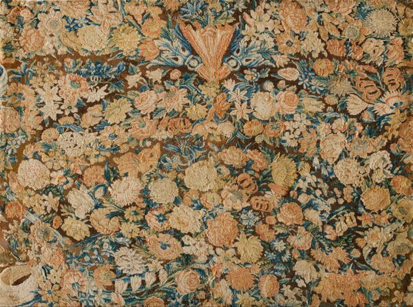 Distressed rug fragment featuring a dense floral pattern in muted cream, peach, blue, and dark brown.