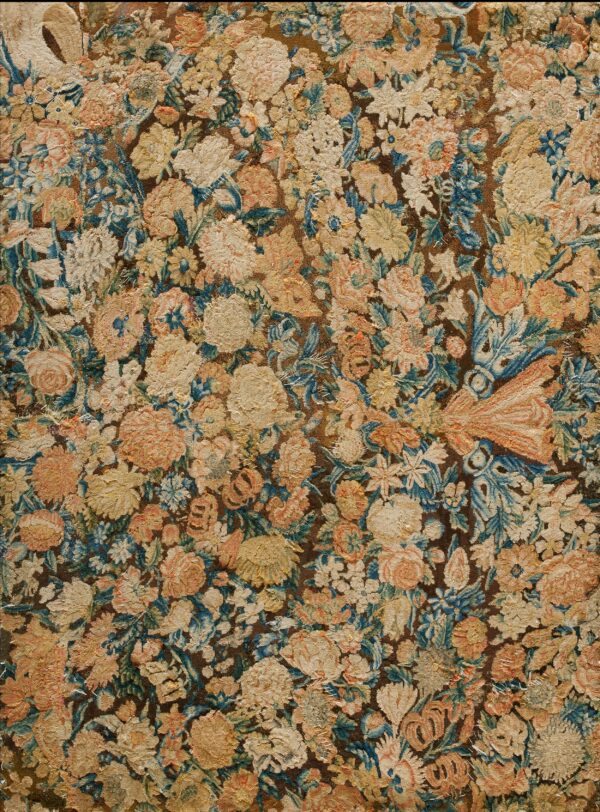 Densely textured rug featuring faded floral designs in cream, yellow, blue, and peach on a dark brown field.