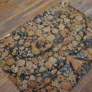 Muted floral tapestry rug with blue, peach, and beige colors shown on distressed wood planks.